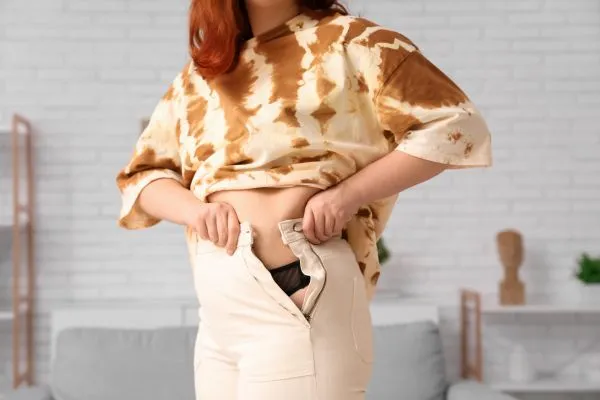 Image of woman trying to do her trousers up after pregnancy weight gain Cannock
