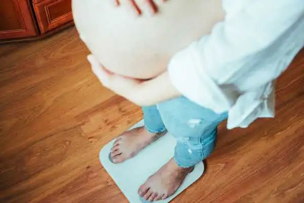 Image of woman weighing herself and experiencing weight gain through pregnancy Cannock